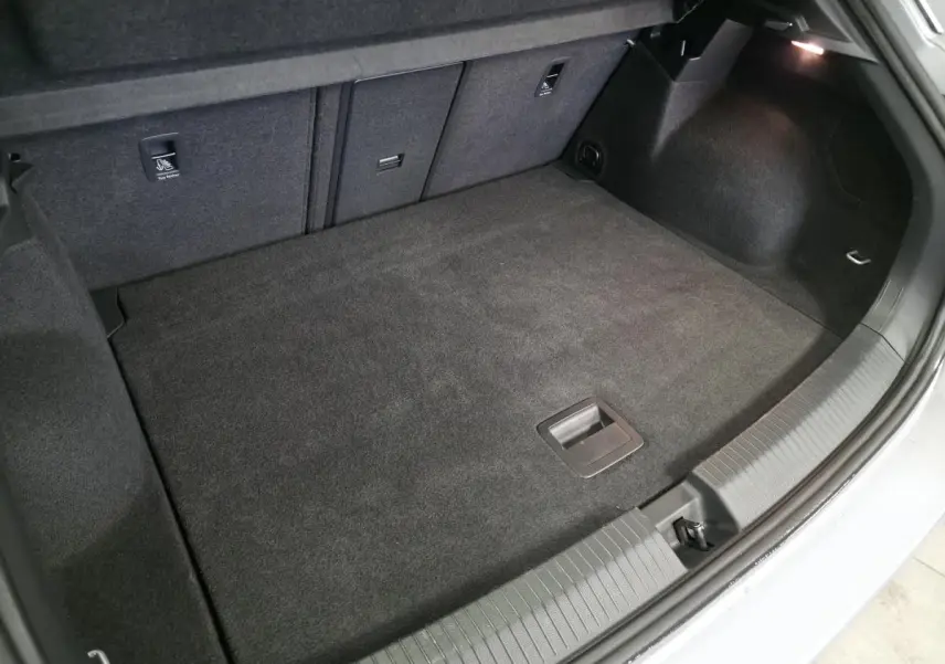 Coffre ouvert vu de l'arrière d'un Volkswagen T-Roc gris, montrant un espace de chargement propre et tapissé.