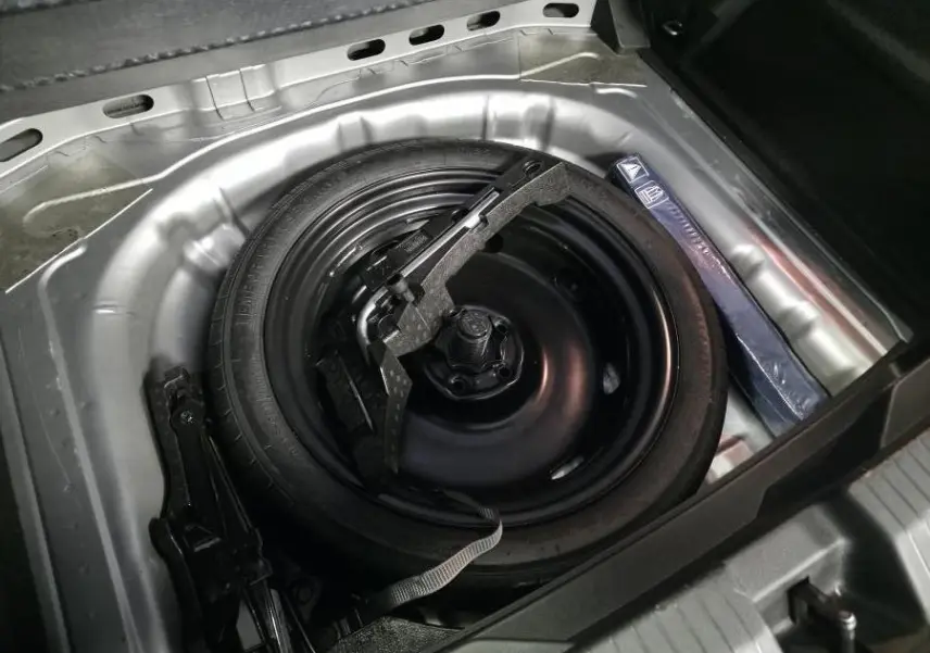 Vue rapprochée de la roue de secours noire et du cric dans le coffre du Volkswagen T-Roc gris 2022.