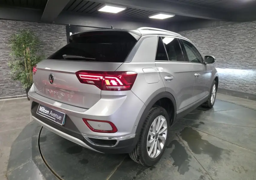 Volkswagen T-Roc gris métallisé vu en 3/4 arrière droit, avec feux arrière LED allumés et vitres surteintées.