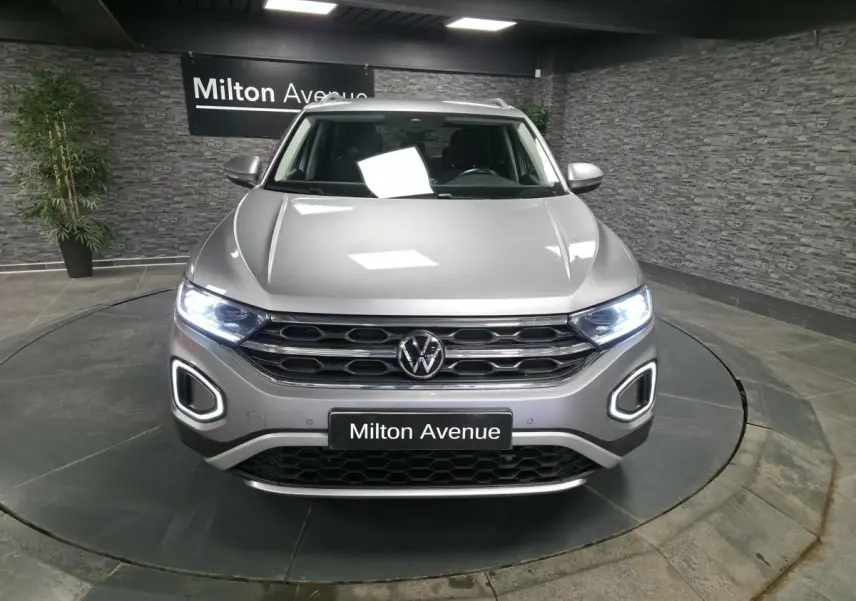 Vue avant d'un Volkswagen T-Roc gris métallisé avec feux LED allumés dans un showroom.