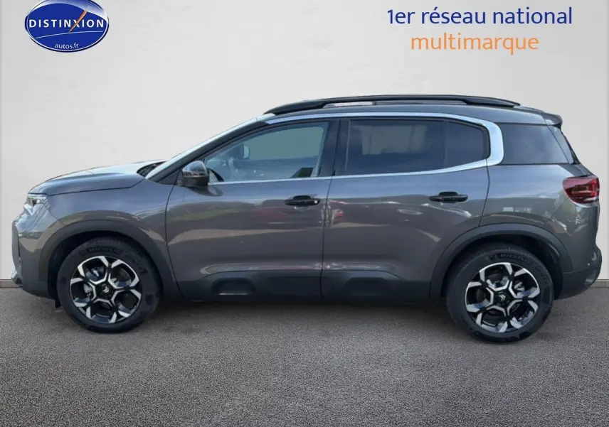 Vue latérale gauche d'un Citroën C5 Aircross gris platinium avec jantes alu et barres de toit noires.