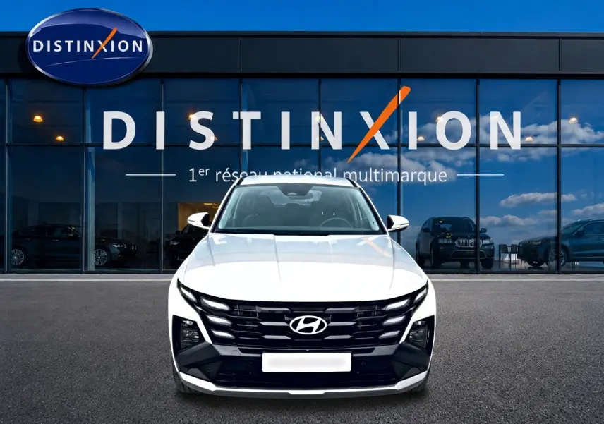 Vue avant d'un Hyundai Tucson blanc 2026 avec calandre noire distinctive, stationné devant une vitrine Distinxion.
