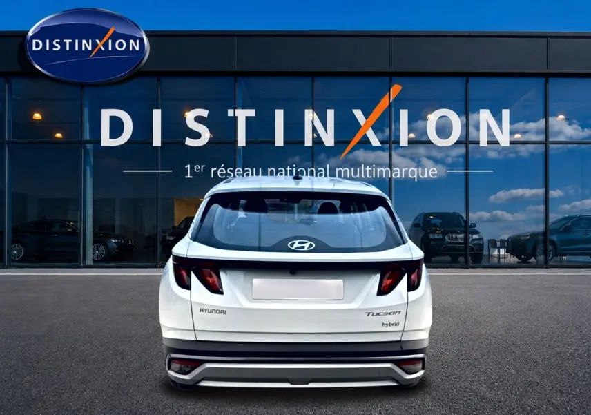 Vue arrière d'un Hyundai Tucson blanc hybride garé devant une vitrine avec logo Distinxion.