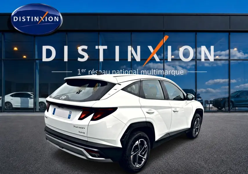 Vue 3/4 arrière droite d'un Hyundai Tucson blanc hybride 2026 avec jantes alliage 17 pouces devant une vitrine Distinxion.