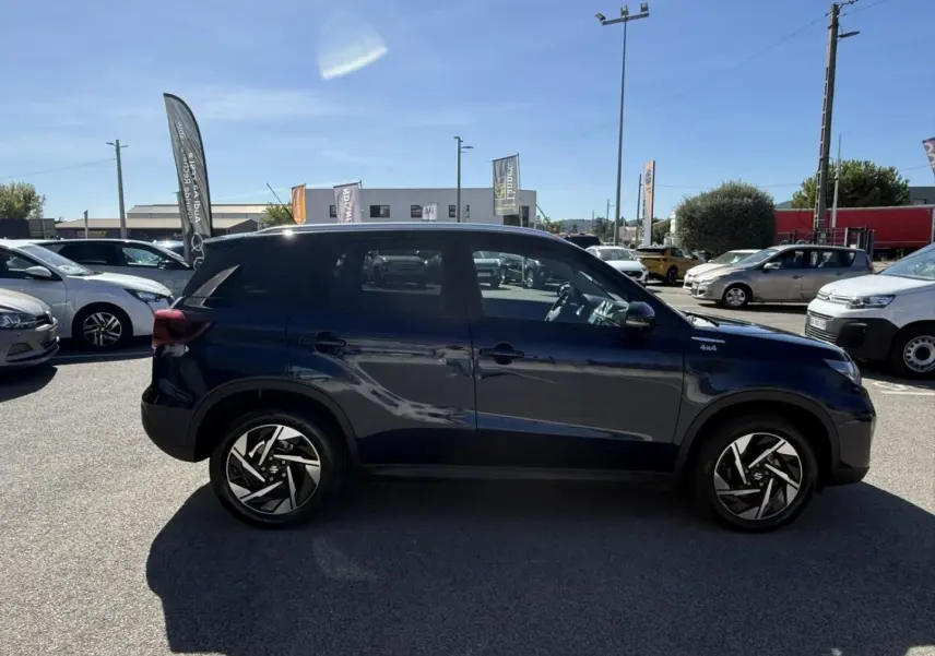 Suzuki Vitara 2025 bleu foncé métal, vue de profil côté gauche, avec jantes alliage noires et badge 4x4 visible.