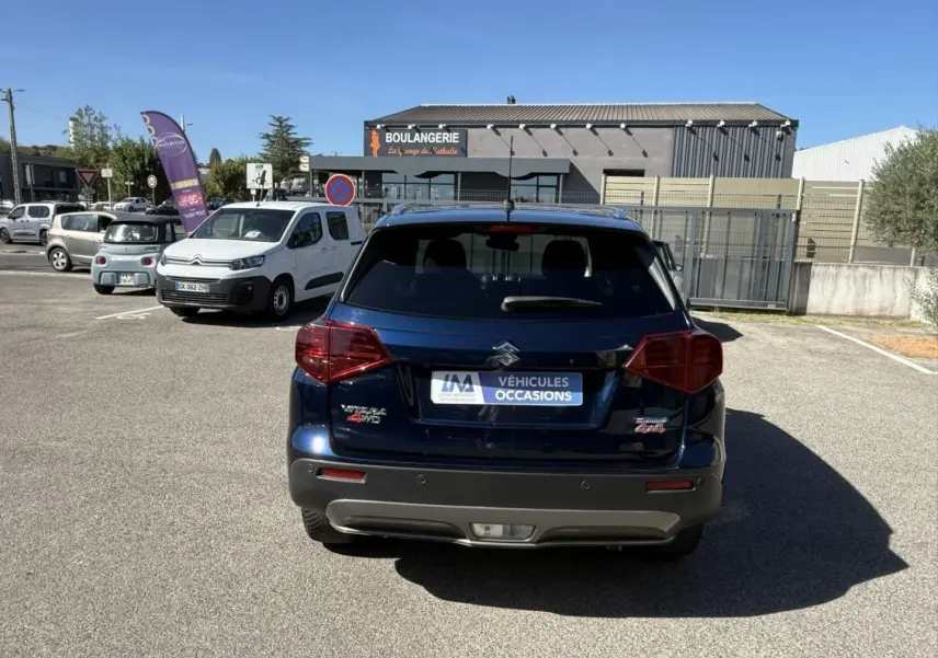 Vue arrière d’un Suzuki Vitara bleu foncé métal 2025 avec badges Allgrip et 4WD sur un parking extérieur.
