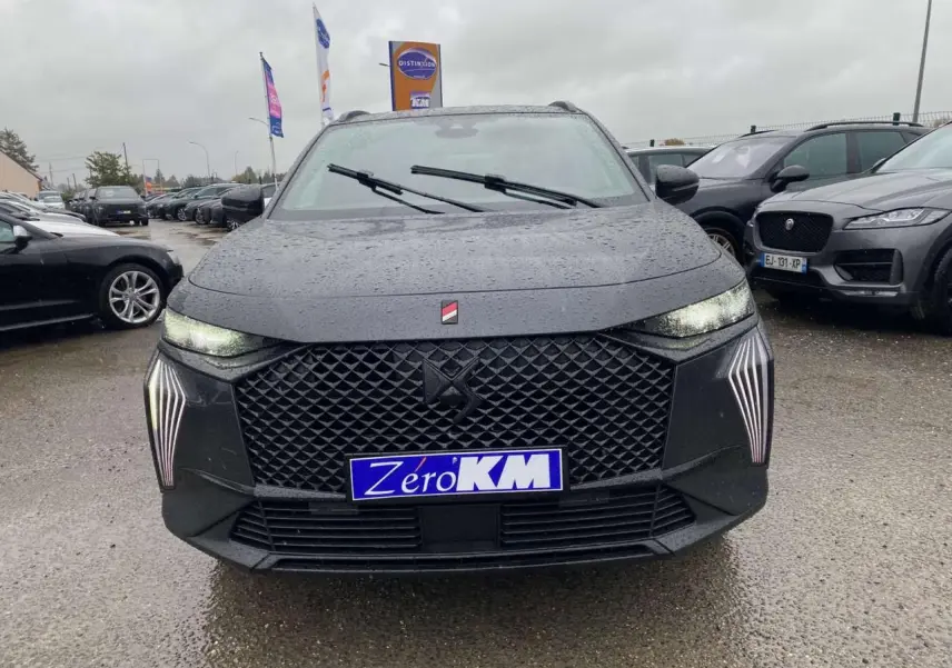 Vue avant d'un DS7 Crossback gris foncé 2024 avec calandre noire et feux LED verticaux allumés sous la pluie.