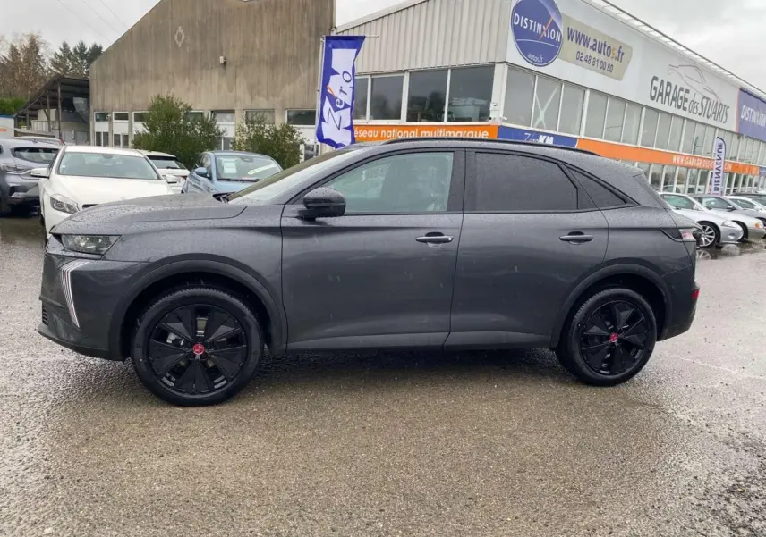 Vue de profil côté gauche du DS7 Crossback gris foncé 2024 avec jantes noires et vitres teintées, sur parking extérieur humide.
