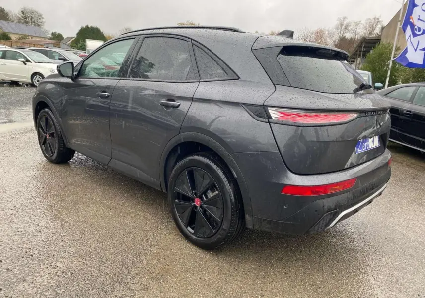 Vue 3/4 arrière droite d’un DS7 Crossback gris foncé 2024 avec jantes noires et feux arrière LED allumés.