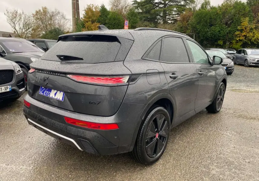 Vue 3/4 arrière droite du DS7 Crossback gris foncé 2024 avec feux arrière allongés et jantes noires distinctives.