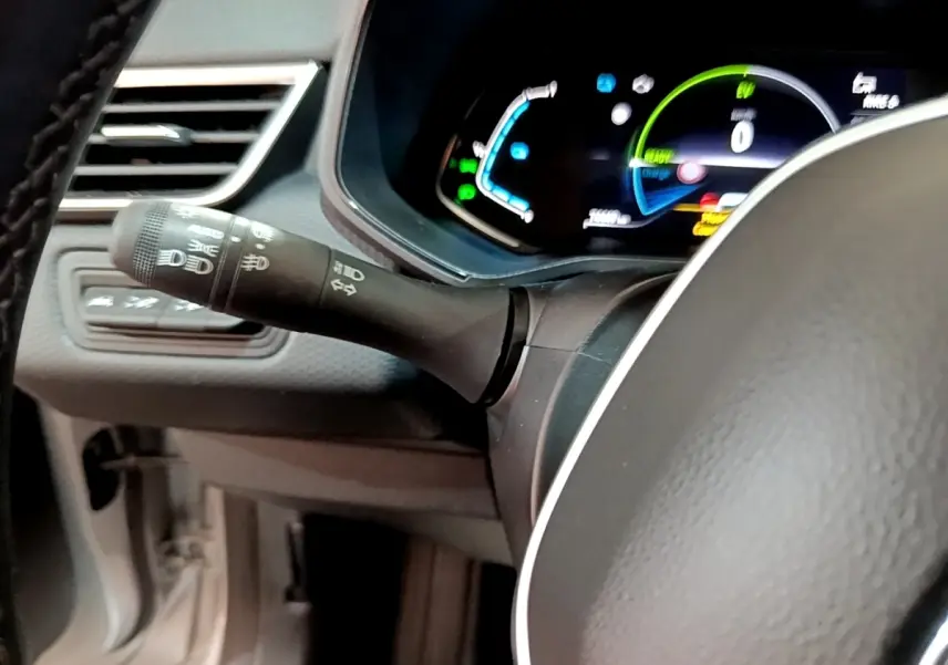 Gros plan sur la manette de commande des phares et clignotants à gauche du volant cuir d’une Renault Clio Business E-TECH 140 gris foncé.