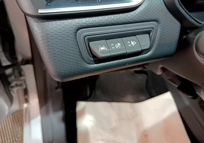 Gros plan sur les commandes d'assistance à la conduite sous le tableau de bord côté gauche de la Renault Clio Business E-TECH 140 gris foncé.