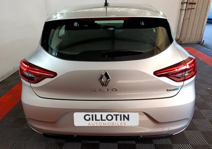 Vue arrière d'une Renault Clio gris clair avec feux LED allumés, dans un garage au sol carrelé noir et orange.