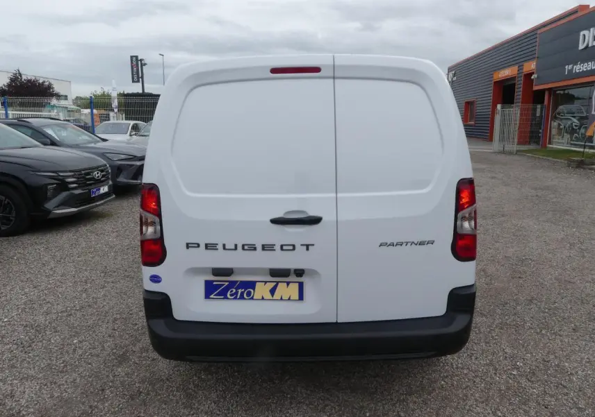 Vue arrière d'un Peugeot Partner blanc 2025 avec portes battantes et logo visible sur un parking extérieur.