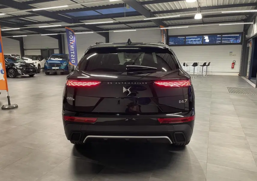 Vue arrière d'un DS7 Crossback noir métallisé avec feux arrière LED allumés dans un showroom.