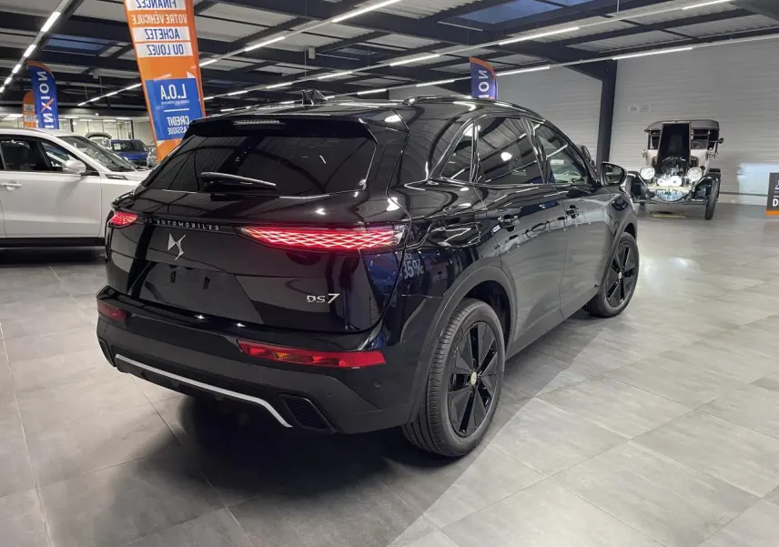 Vue 3/4 arrière droite d'un DS7 Crossback noir métallisé avec feux arrière LED et jantes noires en showroom.