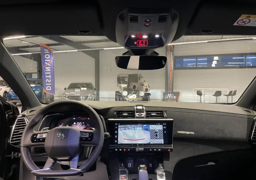 Vue intérieure avant du DS7 Crossback noir métallisé, mettant en valeur le volant cuir perforé et l'écran tactile central affichant la caméra de recul.