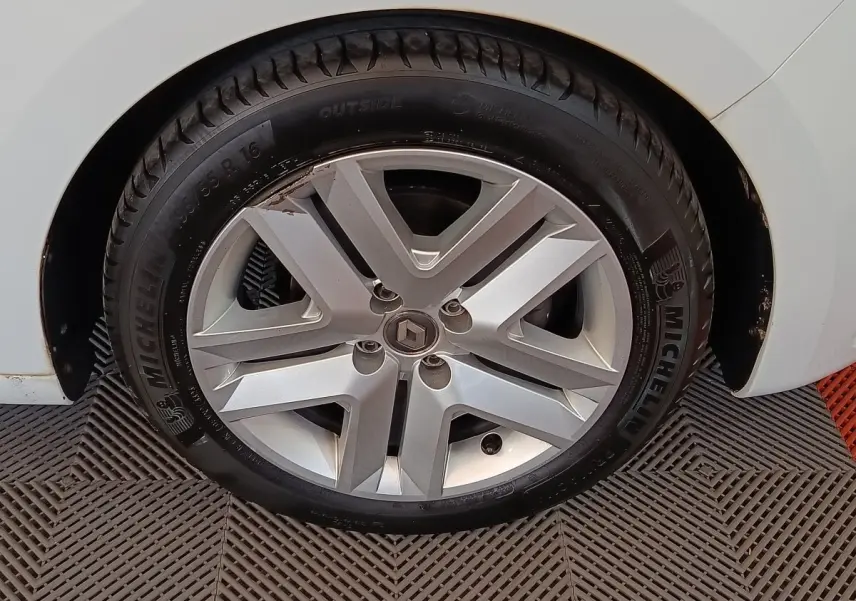 Gros plan sur la roue avant droite d’une Renault Clio blanche, avec jante alliage et pneu Michelin visible.