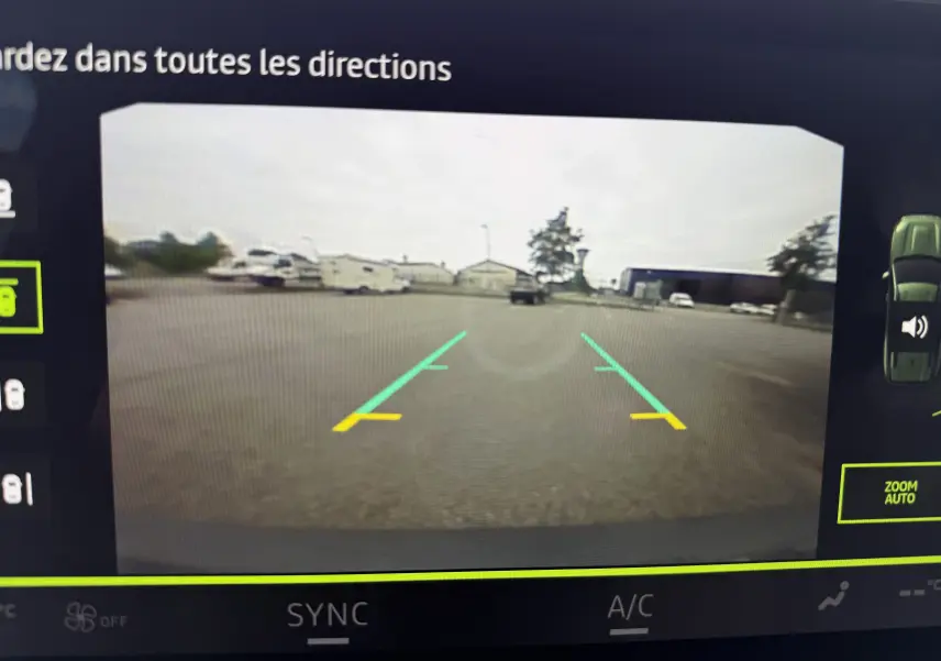 Vue caméra de recul du Dacia Bigster gris schiste, affichant les lignes de guidage sur un parking dégagé.