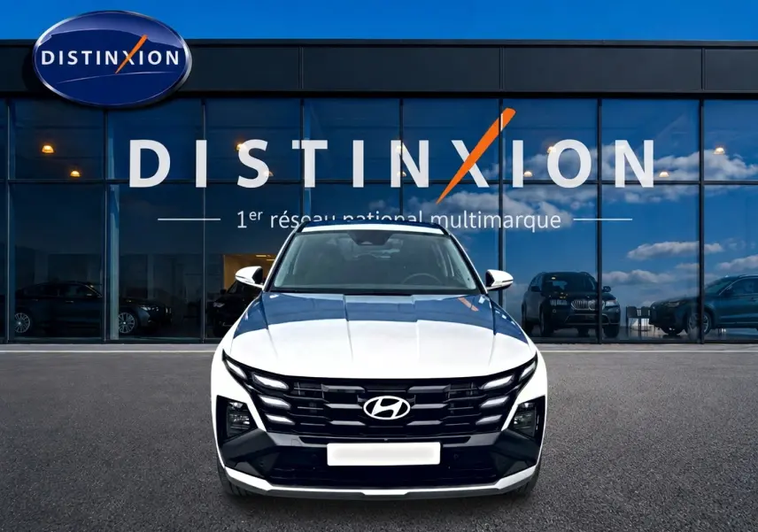 Vue frontale d'un Hyundai Tucson blanc 2026 avec calandre noire et logo Hyundai bien visible, devant une vitrine Distinxion.