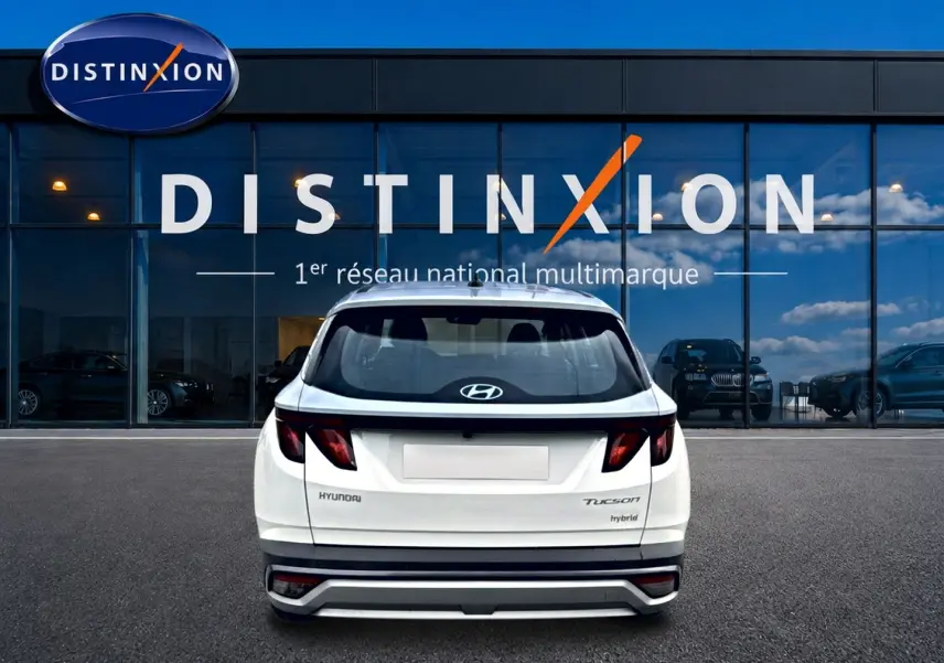 Vue arrière d'un Hyundai Tucson hybride blanc 2026 garé devant une vitrine avec logo Distinxion.