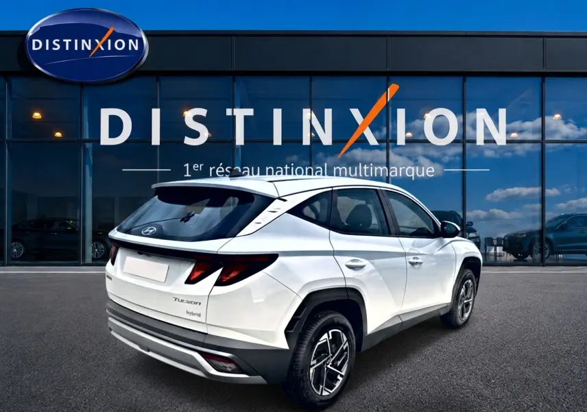 Vue 3/4 arrière droite d'un Hyundai Tucson blanc hybride 2026 devant une vitrine Distinxion.