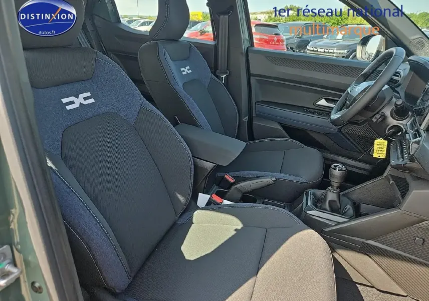 Intérieur avant droit du Dacia Duster 2025 vert kaki, sièges tissu noir et bleu avec accoudoir central et boîte manuelle.