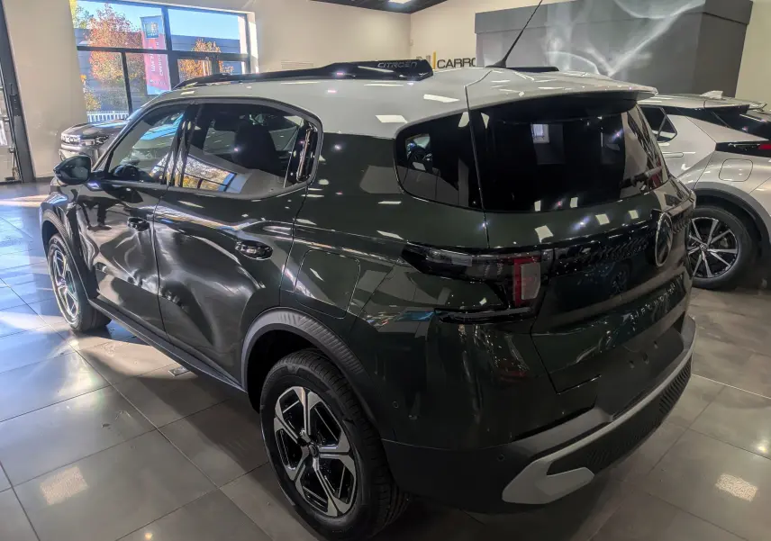 Vue 3/4 arrière droite d'un Citroën C3 Aircross 2025 vert Montana avec toit blanc en showroom lumineux.