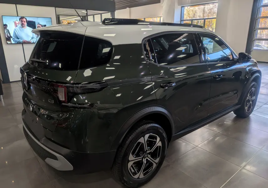 Vue 3/4 arrière droite d'un Citroën C3 Aircross hybride vert Montana avec toit blanc en showroom.