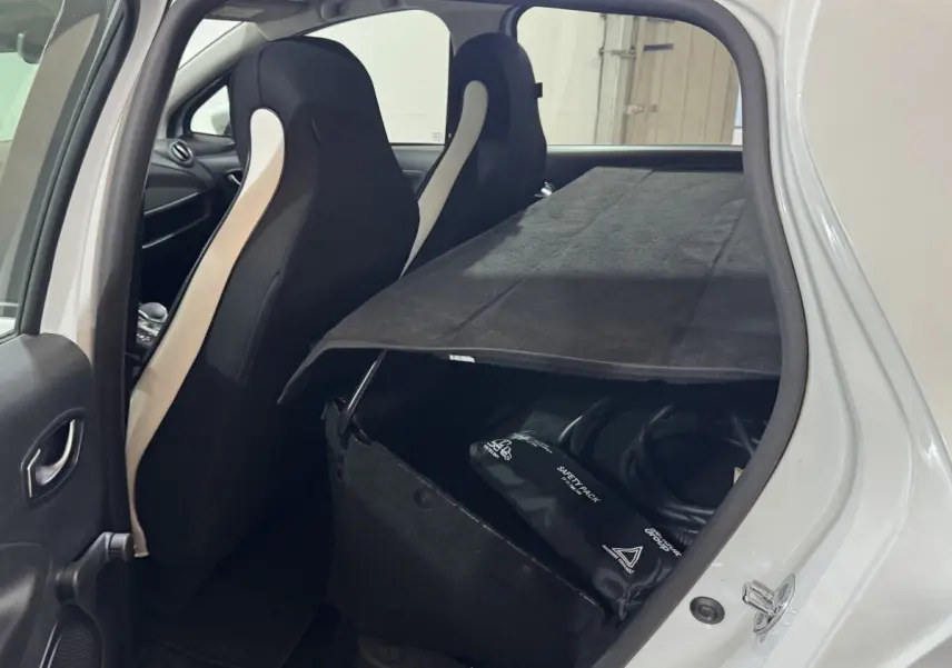 Vue intérieure arrière gauche d'une Renault ZOE blanche 2020, montrant les sièges avant et un rangement avec câble de recharge.