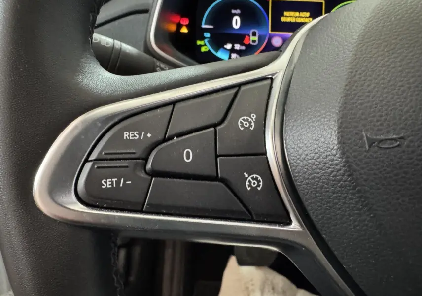 Gros plan sur les commandes du régulateur de vitesse au volant cuir de la Renault ZOE Business blanc 2020.