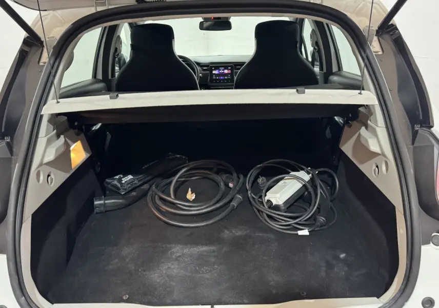 Coffre ouvert d’une Renault ZOE blanche vue de l’arrière, avec câbles de recharge électrique visibles à l’intérieur.