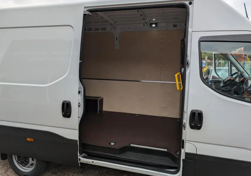Vue latérale droite d’un Iveco Daily blanc 2025 avec porte coulissante ouverte montrant l’espace de chargement vide et habillé.