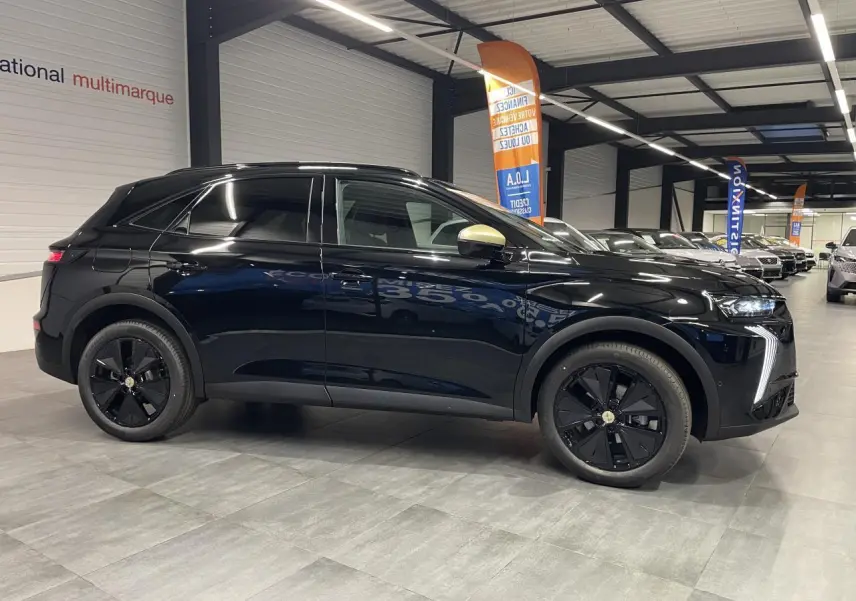 Vue de profil côté gauche d’un DS7 Crossback noir métallisé avec jantes noires et rétroviseurs dorés satinés en intérieur showroom.
