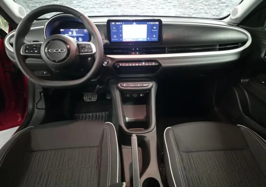 Vue intérieure avant de la FIAT 600 rouge 2024, tableau de bord noir mat avec écran tactile central et volant multifonction.