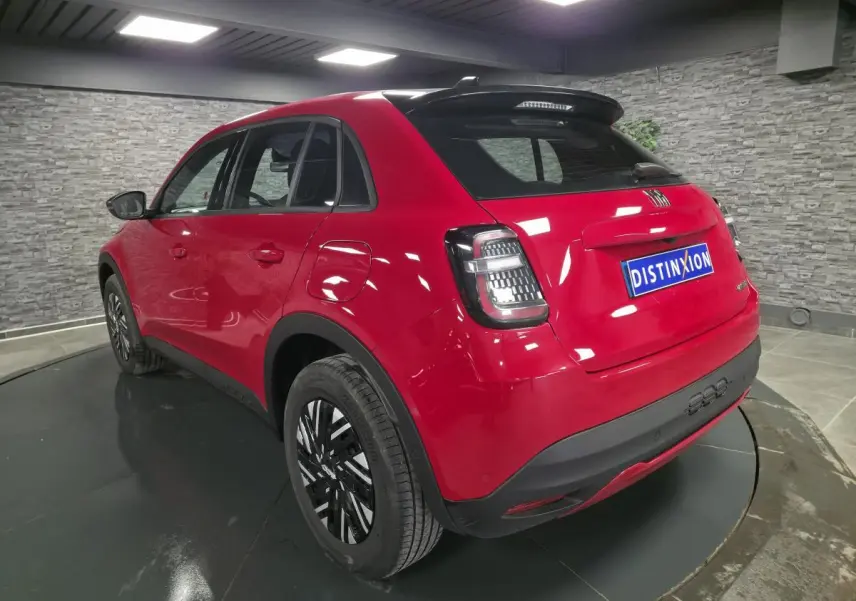 Vue 3/4 arrière droite d'une FIAT 600 rouge 2024 avec jantes bicolores et toit noir brillant.