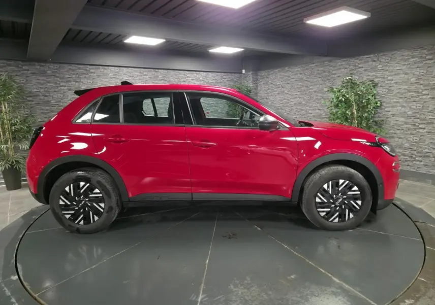 Vue de profil côté gauche d'une FIAT 600 rouge 2024 avec jantes bicolores et coques de rétroviseurs noires.