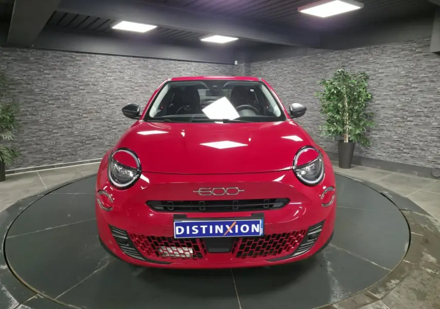 Vue avant d'une FIAT 600 rouge brillante avec logo 600 et calandre noire dans un showroom.