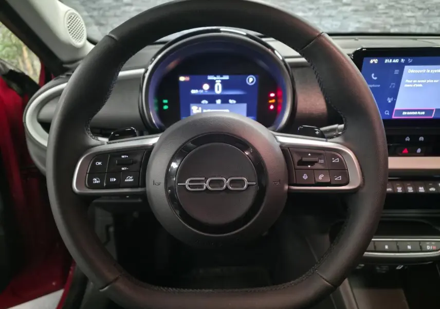 Vue centrée sur le volant noir de la FIAT 600 rouge 2024 avec tableau de bord numérique et écran tactile.