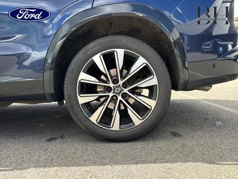 Gros plan sur la roue arrière droite d'un véhicule bleu avec jante alliage noir et argentée, logo Renault au centre.