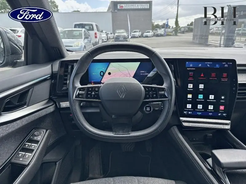 Vue intérieure centrée sur le volant multifonction et l'écran tactile du tableau de bord du Renault Espace rouge 2024.