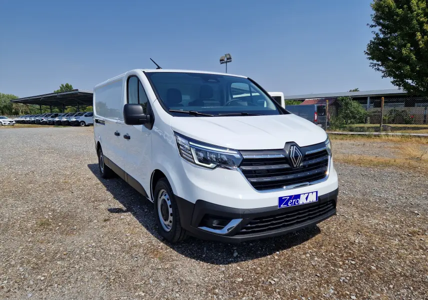 Renault Trafic Fourgon blanc en 3/4 avant droit, avec calandre noire et phares LED distinctifs, sur parking extérieur.