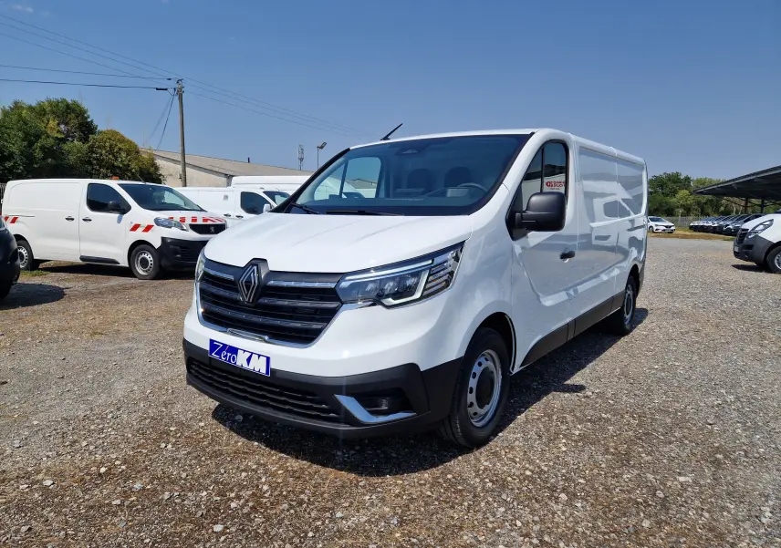 Renault Trafic Fourgon blanc vu en 3/4 avant droit sur parking, avec calandre noire et phares LED distinctifs.