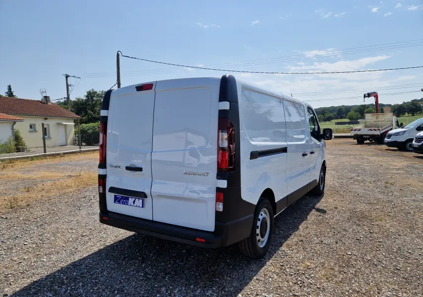 Renault Trafic Fourgon blanc vu en 3/4 arrière droit sur un terrain gravillonné par temps ensoleillé.