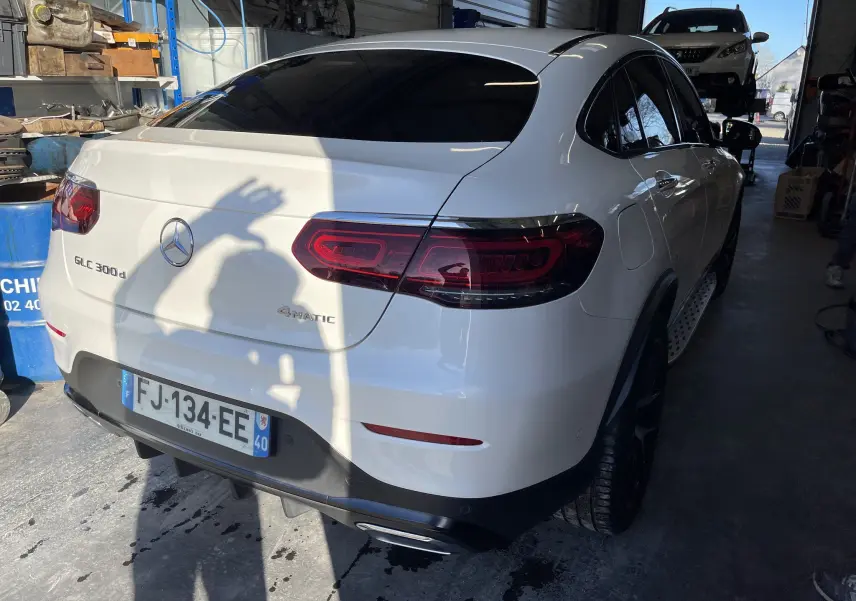 Vue 3/4 arrière droite d'un Mercedes GLC Coupé blanc 300 d AMG Line avec feux LED et badge 4MATIC visible.