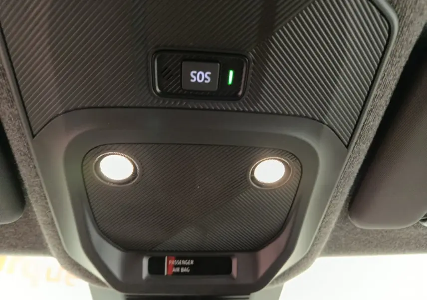 Vue en contre-plongée du plafonnier intérieur noir avec bouton SOS éclairé et deux lampes allumées dans une Renault R5 blanche électrique.