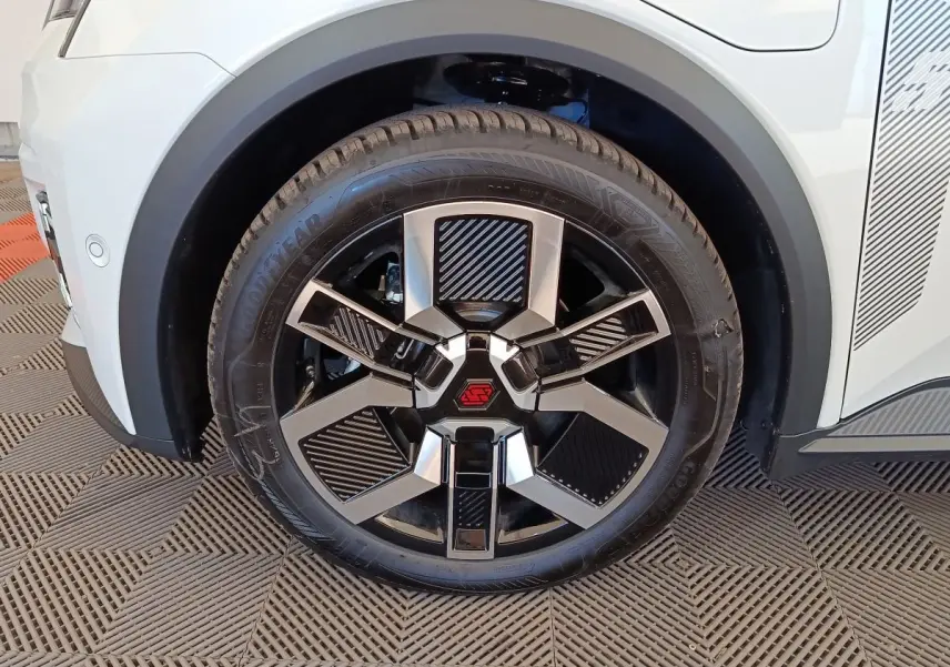 Gros plan sur la roue avant gauche de la Renault R5 Techno blanche, avec jante noire et argent au design géométrique.