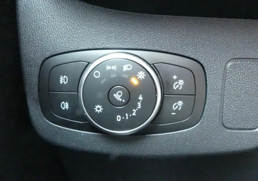 Gros plan sur la molette de réglage des phares et des feux du tableau de bord noir du Ford Puma blanc.