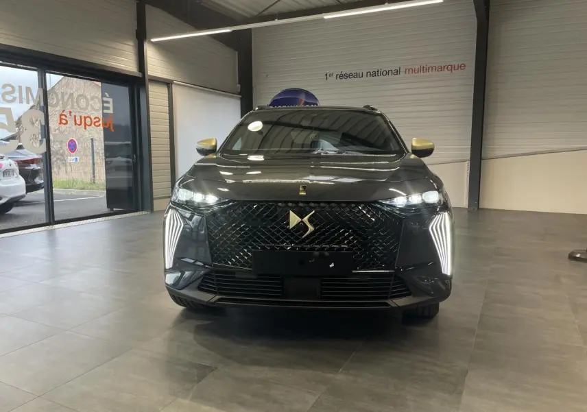 Vue frontale du DS7 Crossback gris titanium avec calandre DS Wings noir brillant et feux LED verticaux allumés.