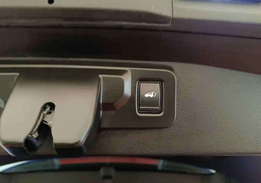 Bouton d'ouverture électrique du coffre sur panneau intérieur noir du Renault Symbioz bleu, vue rapprochée.